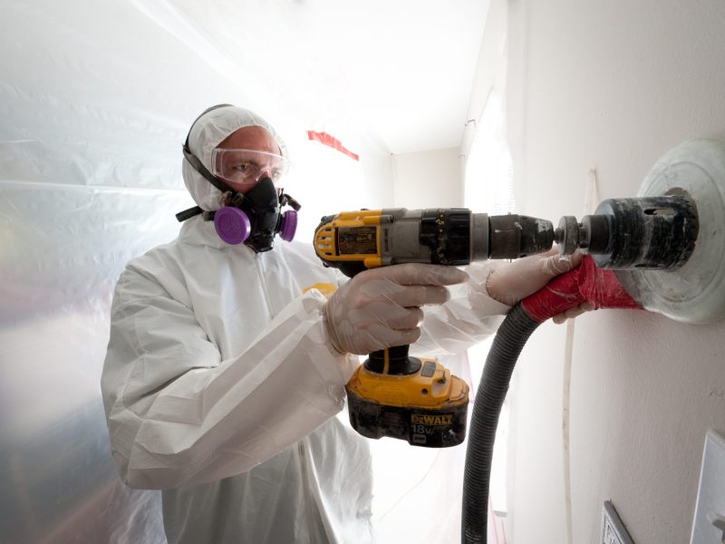 A weatherization worker drills holes to blow cellulose insulation in the interior walls of a Colorado home.