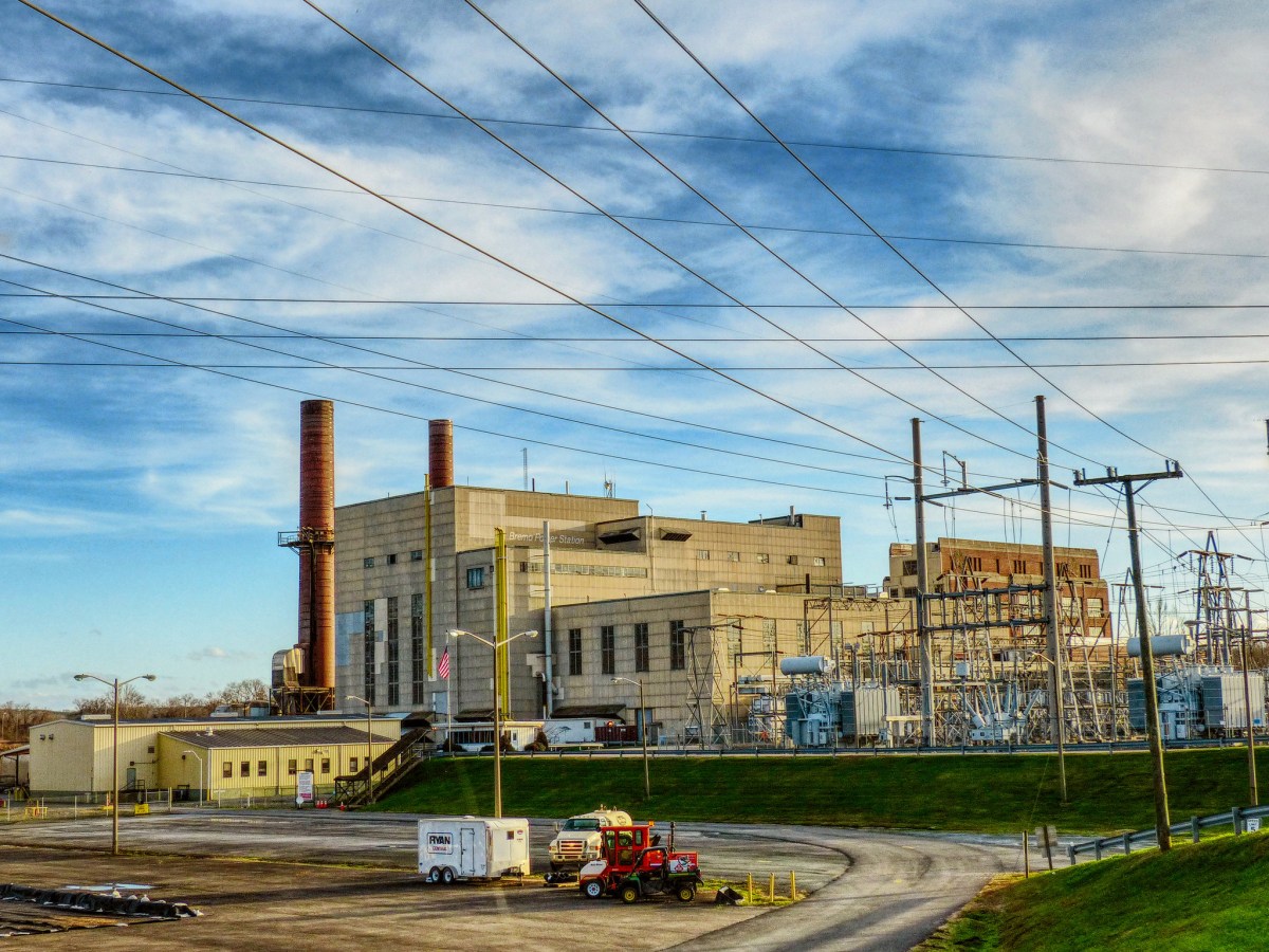 A large power plant and attached substation stand against a blue sky.