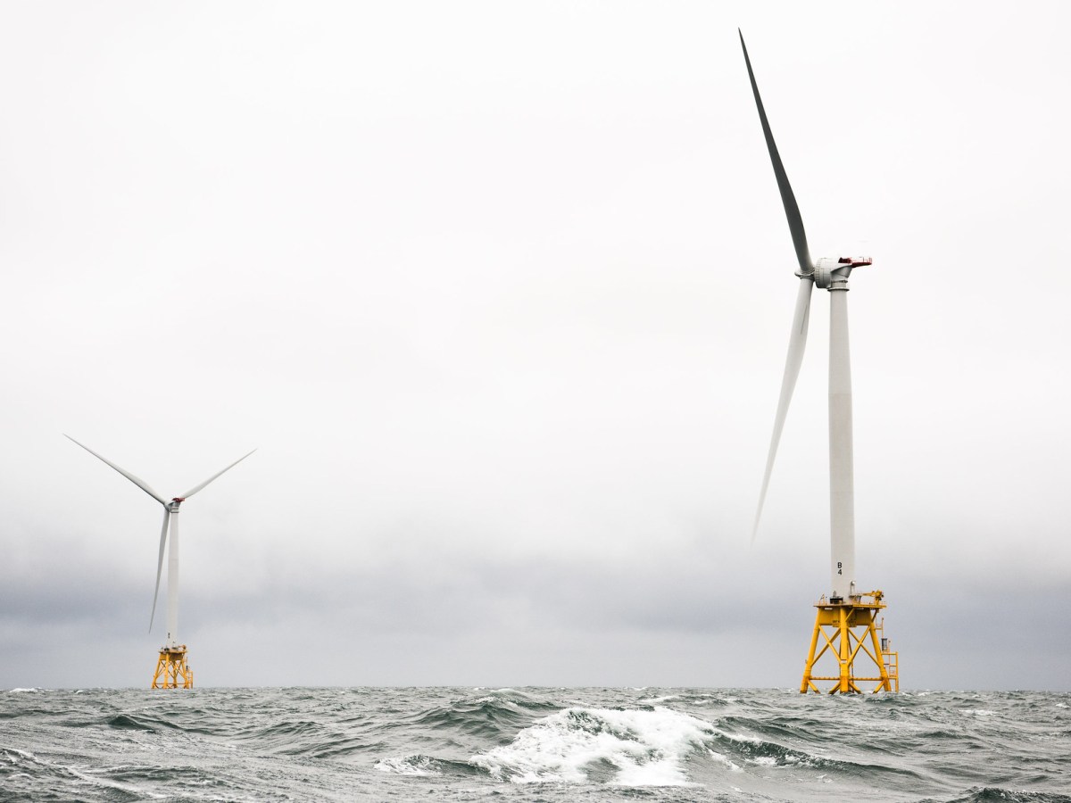 Two offshore wind turbines sit in grey churning water against a great sky