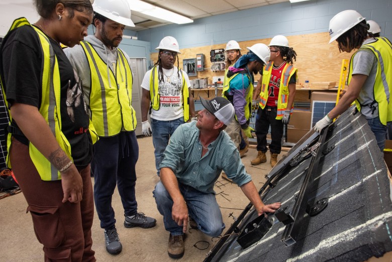 Students gather around an instructor explaining a solar mounting bracket.