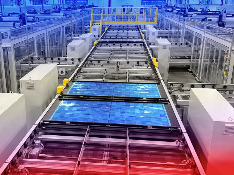 A factory filled with clean white structures produces solar panels, visible in blue at the front of the picture.