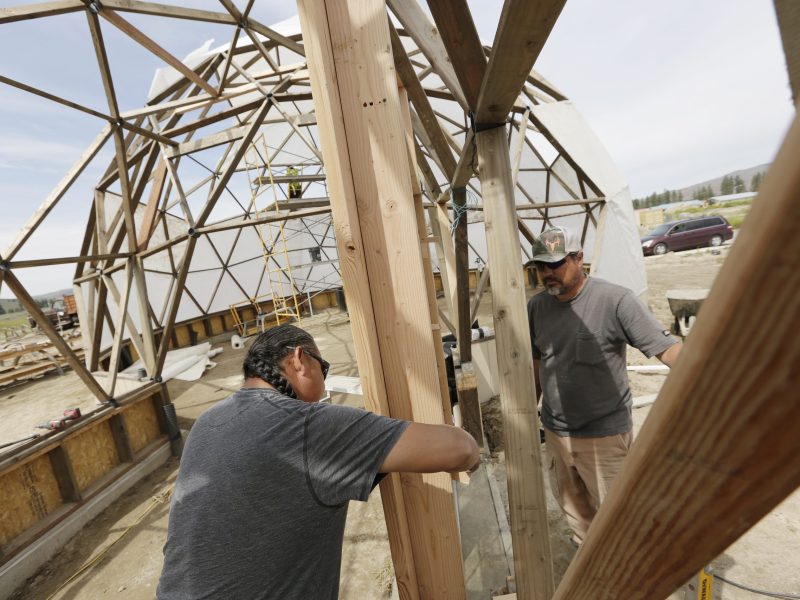 Ricky Gabriel, owner of Gabriel Construction and Development and strategic infrastructure partner with Konbit, left, and Doublas Lucht, trainee at Tribal Employment Rights Organization, install a door on a geodesic dome on Wednesday, June 15, 2022, in Nespelem, Washington.