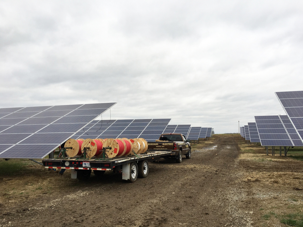 A pickup truck pulling a trailer with spools of wire on it drives through a nearly completed solar array.