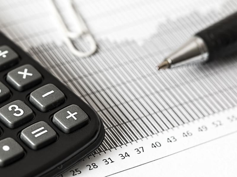 Closeup of a calculator and pen resting on top of a paper with a bar chart.