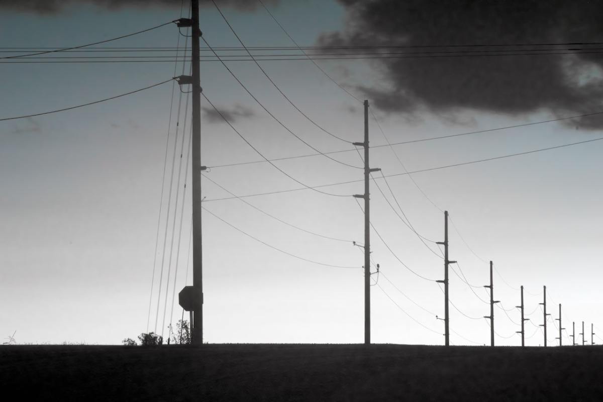 A long line of silhouetted electric posts disappearing into the distance.