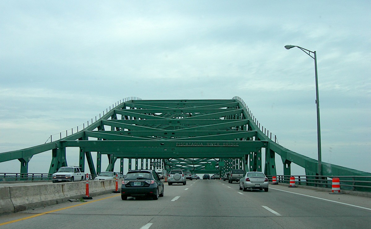 Cars travel across a highway bridge topped with a green girder structure