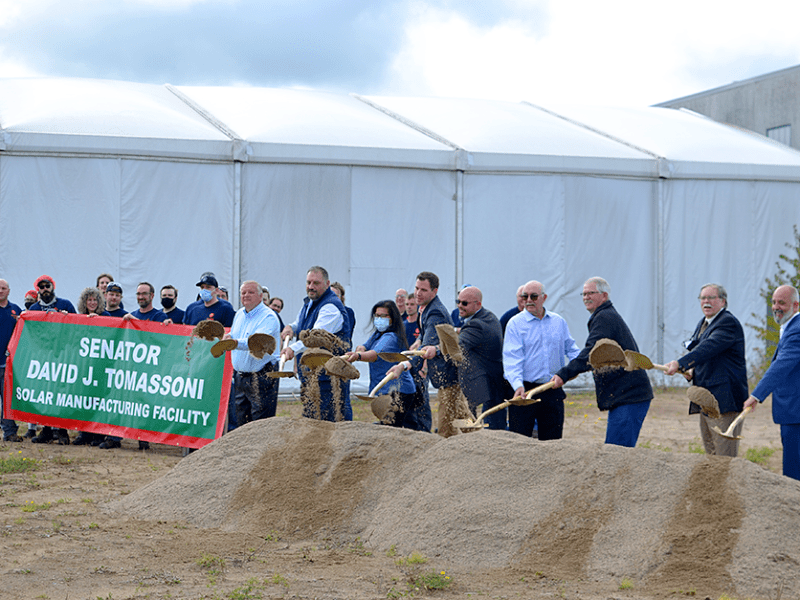 A group of people shovel a pile of dirt in a groundbreaking ceremony for a major solar panel factory expansion